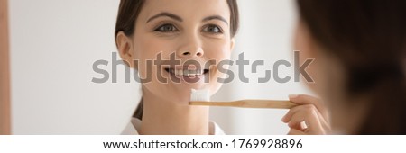 Head shot close up mirror reflection smiling beautiful young woman holding bamboo eco toothbrush, standing in bathroom, attractive girl choosing eco-friendly product for oral hygiene wide image