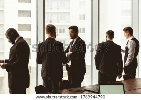 Silhouettes of people against the window. A team of young businessmen working and communicating together in an office. Corporate businessteam and manager in a meeting.