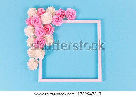 White square shaped picture frame surrounded by pink and white foam rose flower blossoms on blue background