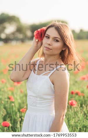 Portrait of a beautiful girl having fun among the red flowers on the poppy field. Young woman smiling and holding a flower in her hands on the sunset. life style. happiness concept.