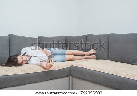 adorable boy on the sofa is playing on the laptop and cell phone