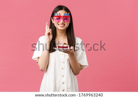 Celebration, party holidays and fun concept. Smiling happy birthday girl making wish on b-day cake, close eyes and cross fingers good luck, want dream come true, pink background