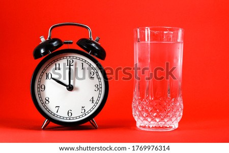 Alarm clock and a glass of water on a red background
