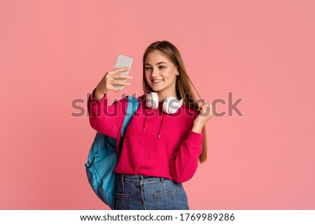 Teen girl with backpack makes selfie on pink background