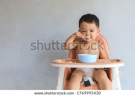 Happy infant Asian baby boy eating food by himself on baby high chair and making mess with copy space. Royalty-Free Stock Photo #1769995430