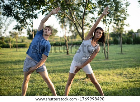 Fit young man and woman exercising in park. Smiling couple doing workouts on grass on sunny morning. Sport couple. Fitness. Photo. 