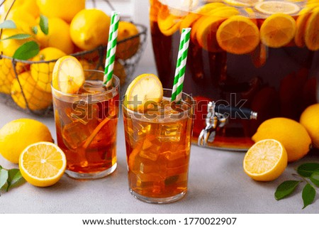 Ice tea, lemonade in glass and beverage dispenser with fresh lemons. Grey background. Close up.