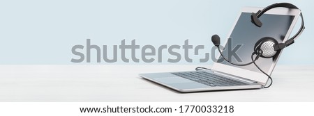 Laptop with blank screen with headphones on desk blue background. copy space. Distant learning or working from home, online courses. Helpdesk or call center headset minimal concept banner Royalty-Free Stock Photo #1770033218