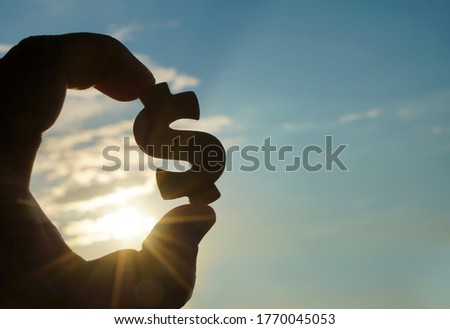 male Hand hold silhouette of dollar sign , symbol of american money against sun rays and sunset sky with clouds. Dollar sign. empty copy space for inscription or other objects.