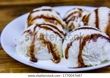 Plate with ice cream balls and chocolate topping on wooden table