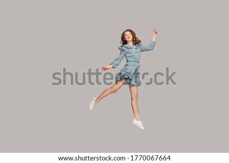 Happy delicate girl in vintage ruffle dress levitating with ballet dance move, hovering in mid-air and smiling joyfully, jumping trampoline, flying up. indoor studio shot isolated on gray background Royalty-Free Stock Photo #1770067664