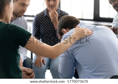 During group therapy session participants supporting crying desperate guy, provide psychological assistance talking encouraging words share mental pain try to help, struggle with addictions treatment Royalty-Free Stock Photo #1770073670