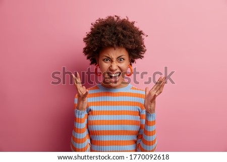 Image of furious outraged woman expresses strong aggression, screams and gestures with anger, wears casual clothes, annoyed by troubles, has misunderstanding and conflict, isolated on pink wall