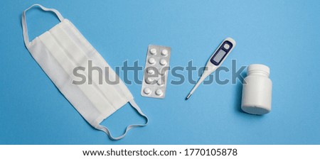 Protective equipment against pandemic, coronavirus, top view. Medical face mask, tablet plate, pills, capsule bottle, thermometer on blue background isolated. Banner for web site