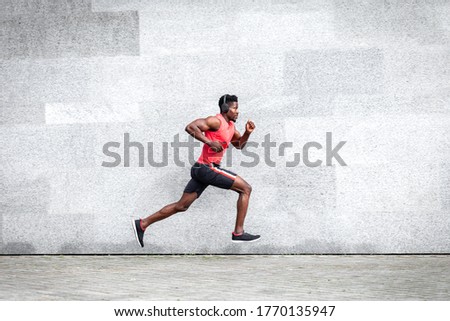 African American guy runner runs fast forward against the background of the city wall, sports man train on the street, general plan Royalty-Free Stock Photo #1770135947