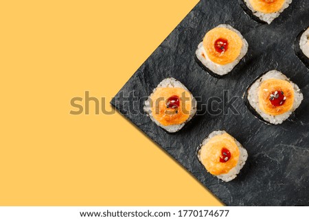 Dish with a set of baked rolls on a yellow background with a copy space. Japanese food concept. Rolls on a black slate dish close up.