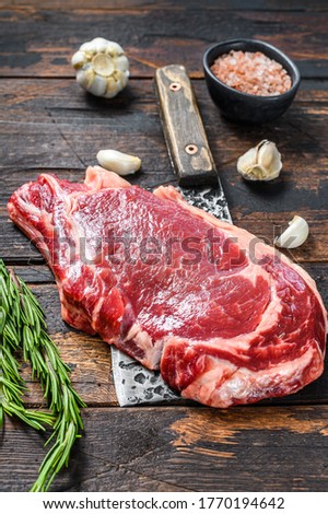 Raw cowboy or rib eye steak on the bone on a meat cleaver. Marble beef meat ribeye. Dark wooden background. Top view