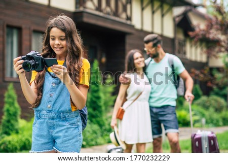 Some new photos. A photo of a family on a weekend, parents hugging and looking at each other, daughter in overalls staying in the foreground, looking at photos in her camera.