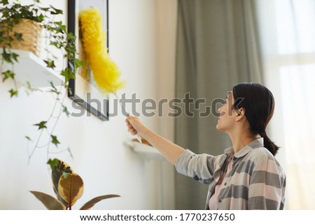 Young woman working at home she wiping dust from pictures on the wall