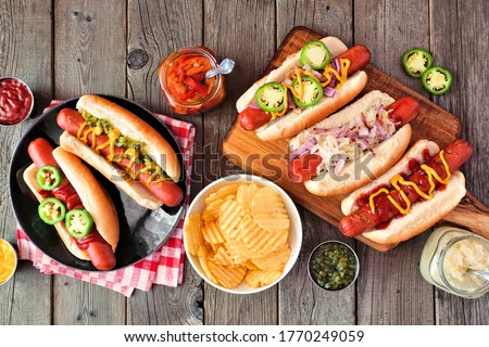 BBQ hot dog table scene. Above view over a dark wood background.