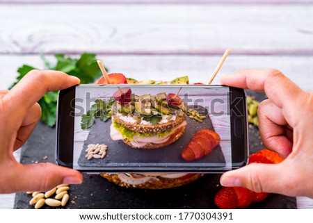 Human hands take a picture to a three-layer sandwich with variety of vegetables, turkey meat and avocado in a whole wheat bread with seeds. Healthy diet concept.