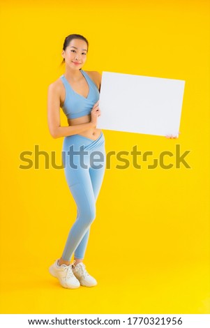 Portrait beautiful young asian woman wear sportwear show empty white billboard on yellow isolated background
