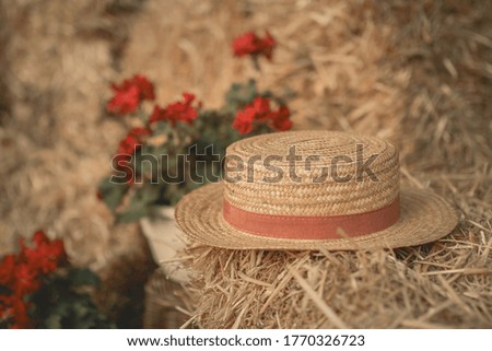 Straw hat on a stack of straw with geranium flowers in the background.
