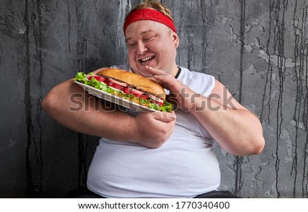 comic caucasian overweight man like this sandwich, holds it in hands and looks at food with love, isolated gray background
