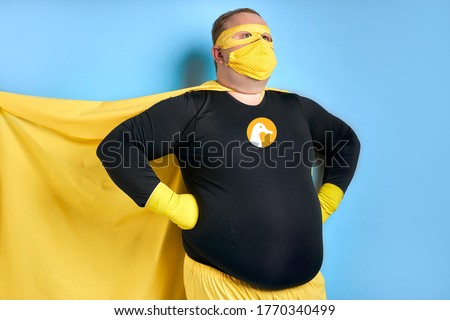 cleaning superhero saves the world from dirt, man has duck picture on costume, he is in yellow wear and in protective gloves, posing isolated over blue background
