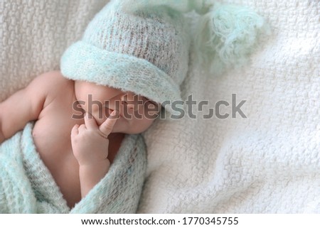 Cute newborn baby in warm hat lying on white plaid, top view. Space for text