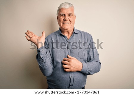 Senior handsome hoary man wearing casual shirt standing over isolated white background smiling cheerful presenting and pointing with palm of hand looking at the camera.