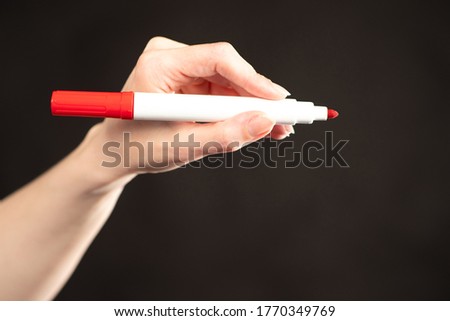 Hand with a red marker on a black background. Red marker next to the text space. Placement of the necessary information. Ad. Advertising.