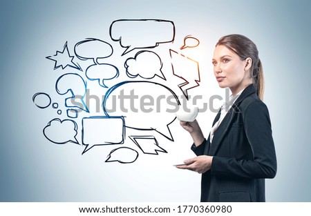 Serious young European businesswoman drinking coffee near gray wall with empty speech bubbles drawn on it. Concept of communication and message delivery