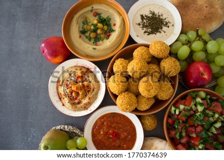 Traditional food of Israel on dark grey background with copy space. Colorful authentic meals top view photo: plate of hummus, falafels, salad, pita bread and tahini sauce. 