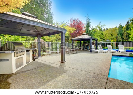 Concrete floor patio area with barbeque, table set, sun chairs and swimming pool