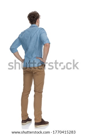 back view of concerned casual guy holding hands on hips and thinking, standing isolated on white background, full body Royalty-Free Stock Photo #1770415283