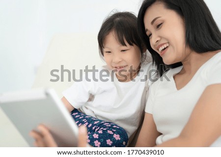 Young mother with children using digital tablet together at home. Smiling family looking at screen, shopping toys or watching cartoon online,