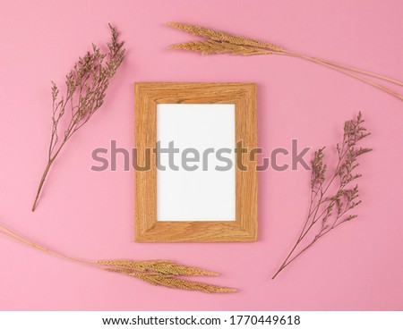 Dried flower and blank wooden photo frame on pastel pink background. Flat lay. Space for text.