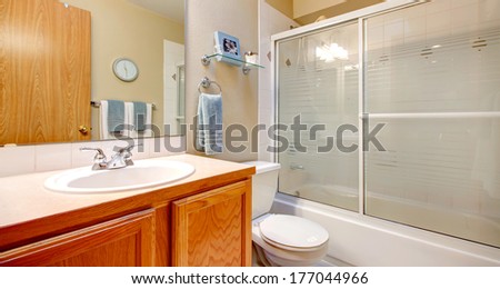 Light tones bathroom with wooden washbasin cabinet, white tub with glass sliding doors