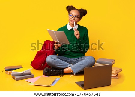 Brainstorming. Pensive black teenage girl doing homework looking upwards over yellow studio background, copyspace