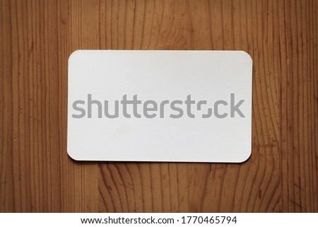 White paper on a wooden texture. White empty business card with round corners in wooden background. Mock-up with white paper on wood.
