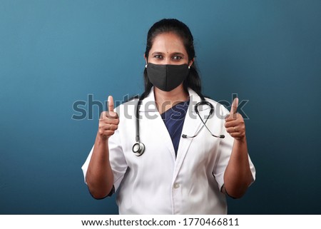 Young female doctor of Indian origin wearing face mask showing thumbs up sign