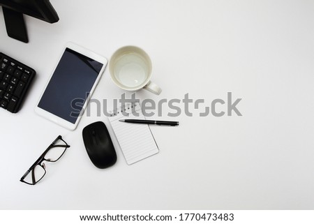 Personal computer, blank screen tablet, book and pen, eye glasses, and a glass of water. Top view, flat lay