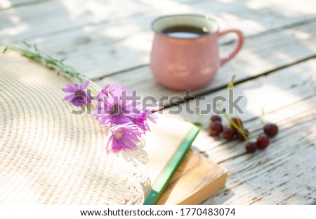 bouquet of flowers, cherry berries, books, cup with a drink and hat on a wooden table in the garden