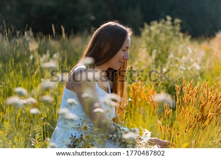 young beautiful woman wit long hair in a white dress and hat among the yellow field of rye and wheat. 
rustic style concept with long hair in a white sundress in a flowering field