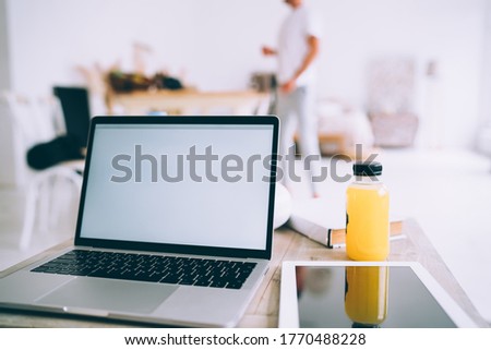Image of laptop computer with mock up screen standing near orange juice and touchpad for freelance online job, modern devices and 4G internet connection at home interior for remote work