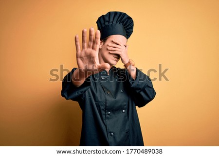 Young beautiful chef woman wearing cooker uniform and hat standing over yellow background covering eyes with hands and doing stop gesture with sad and fear expression. Embarrassed and negative concept