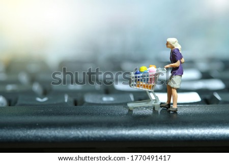 A woman doing online shopping. Walking with cart shop above keyboard. Miniature people figurines toys conceptual photography.