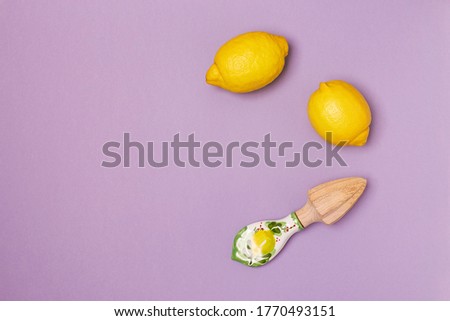 Top view of juicy lemons and a handmade wooden juice squeezer with a beautiful ceramic handle on a purple background