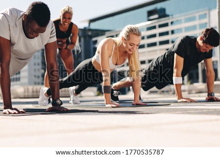 Fitness men and women doing push-ups with motivation from their female trainer outdoors in the city.